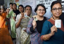 चुनाव प्रचार के दौरान हाथ जोड़े हुए ग्रामीण भारतीय महिलाओं का समूह और पीछे राजनीतिक रैलियों का दृश्य