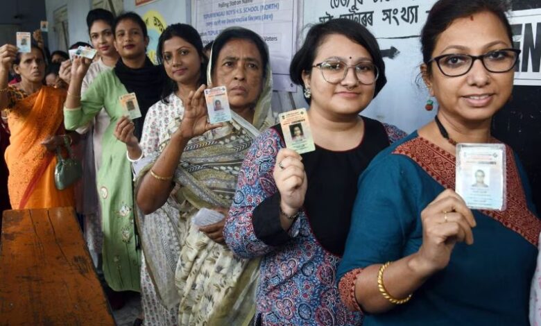 चुनाव प्रचार के दौरान हाथ जोड़े हुए ग्रामीण भारतीय महिलाओं का समूह और पीछे राजनीतिक रैलियों का दृश्य